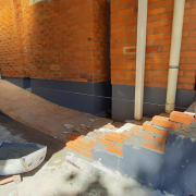 Em um prédio de tijolos à vista, vê-se uma escada de cinco degraus que está sendo reformada com novos tijolos.